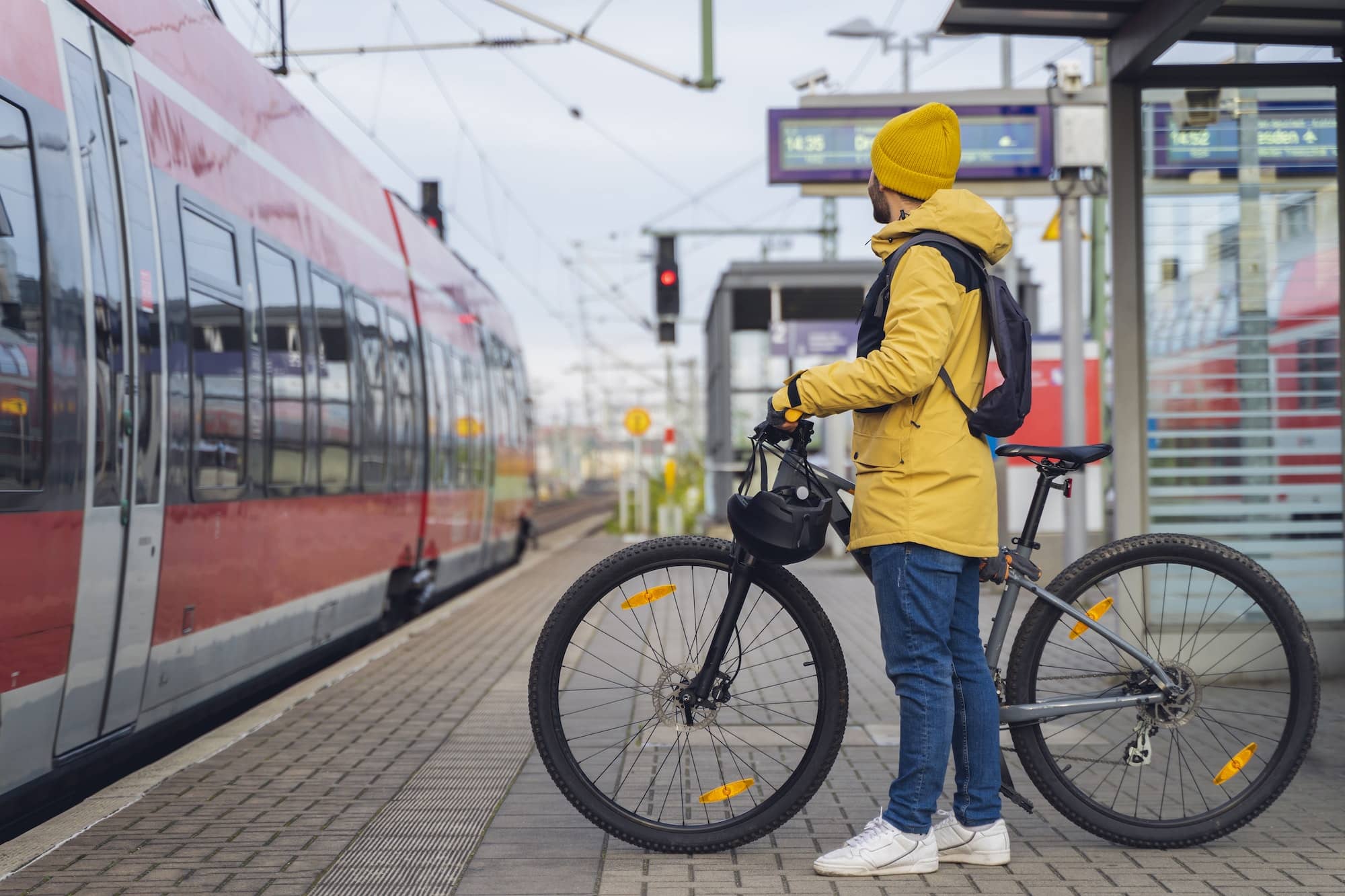 A man, wearing winter clothes, at the station, is about to get on the train, with his bicycle.