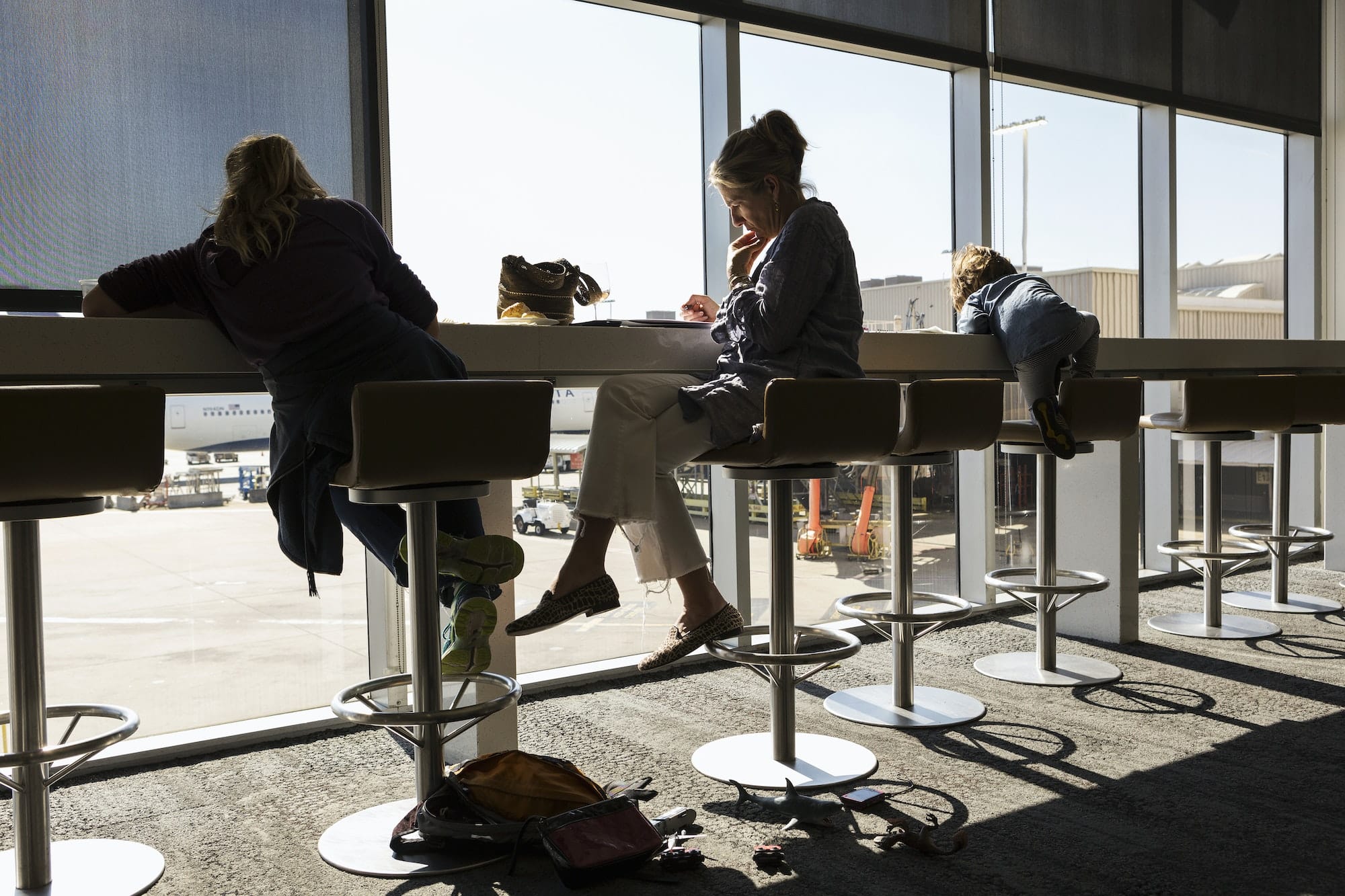 A mature woman and two children seated on high stools at an airport departure lounge