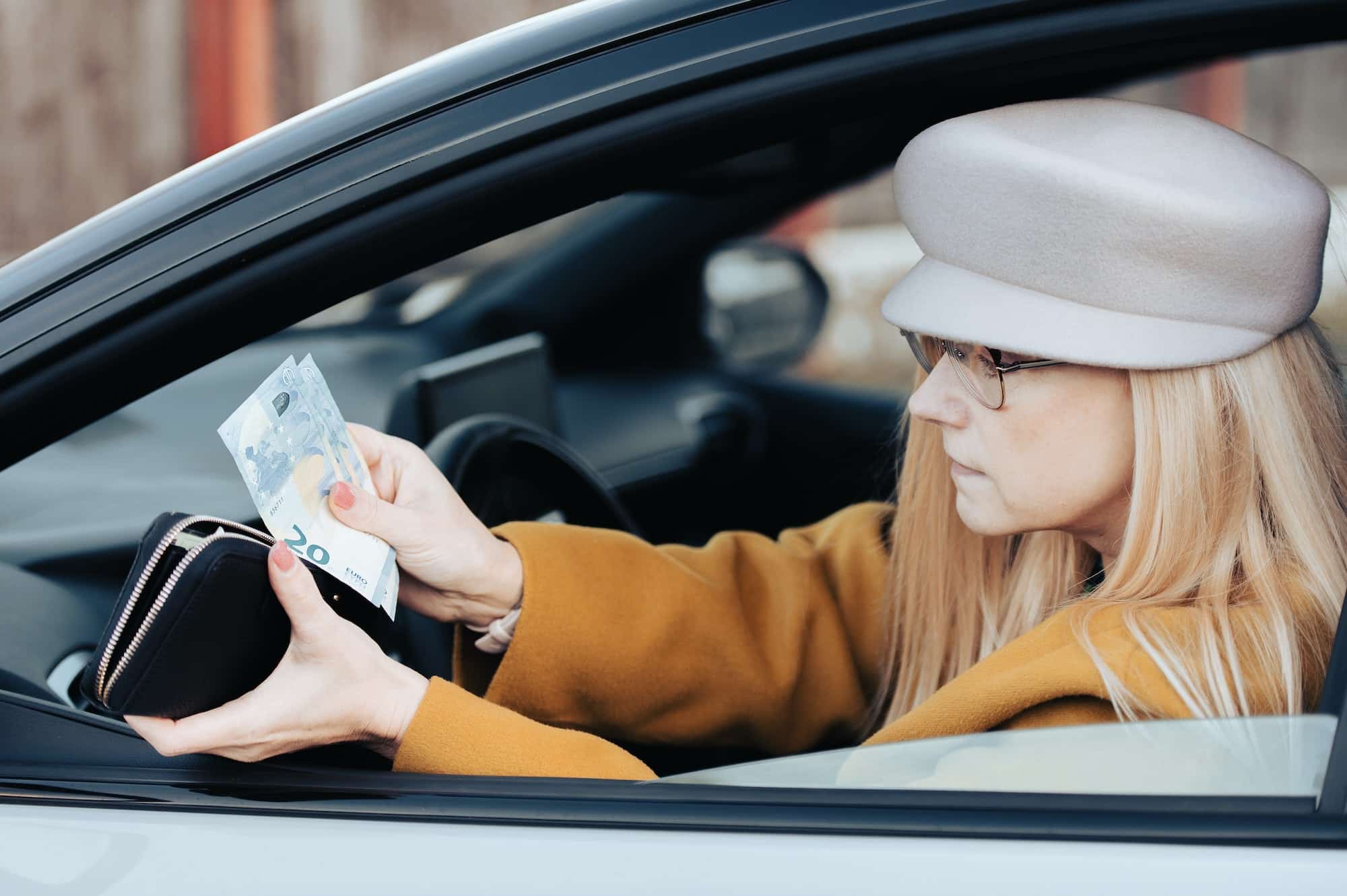 Middle-aged woman sits behind the wheel of car and looks for euro in wallet to pay for parking