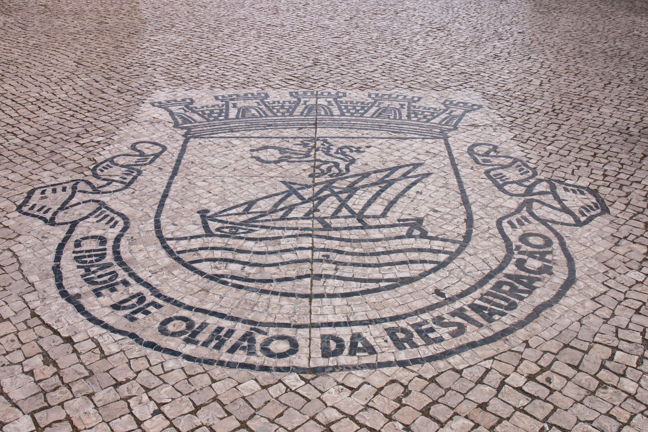 Coat of arms of Olhao city, Portugal over a cobblestone street.