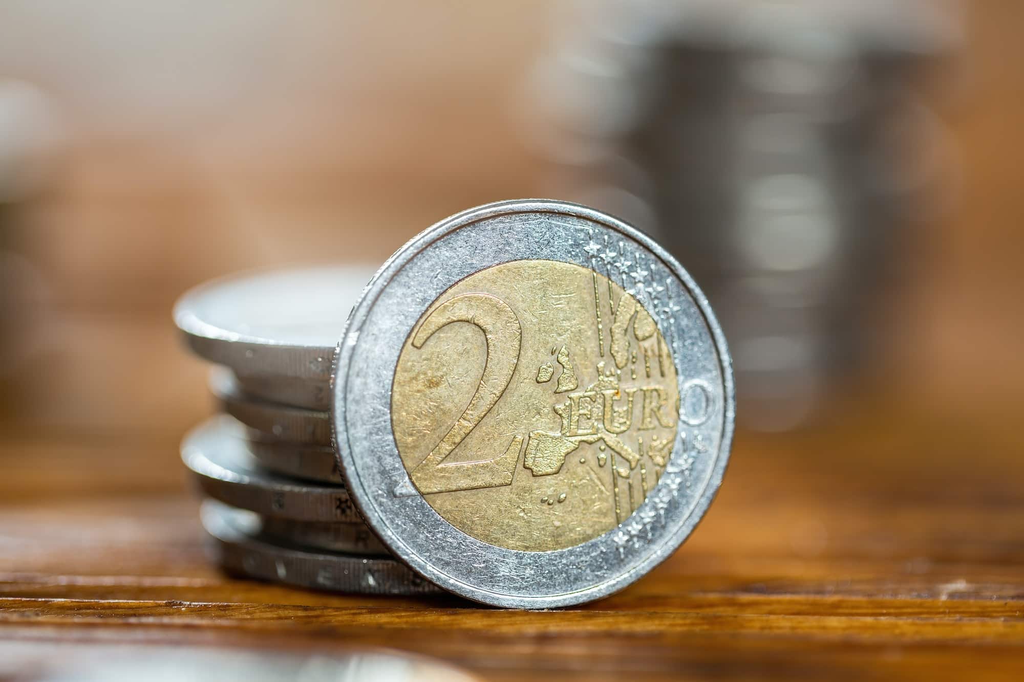 Scratched two euro coin from close-up with piles of money in background