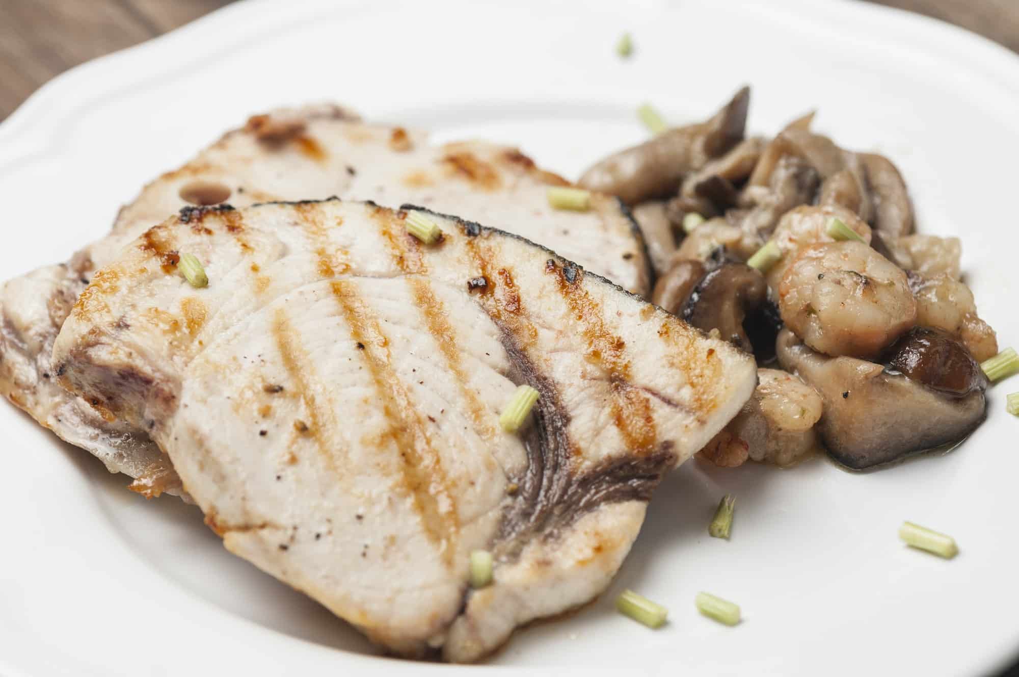 Closeup shot of grilled Emperor Fish fillets with mushrooms and prawns on a white plate