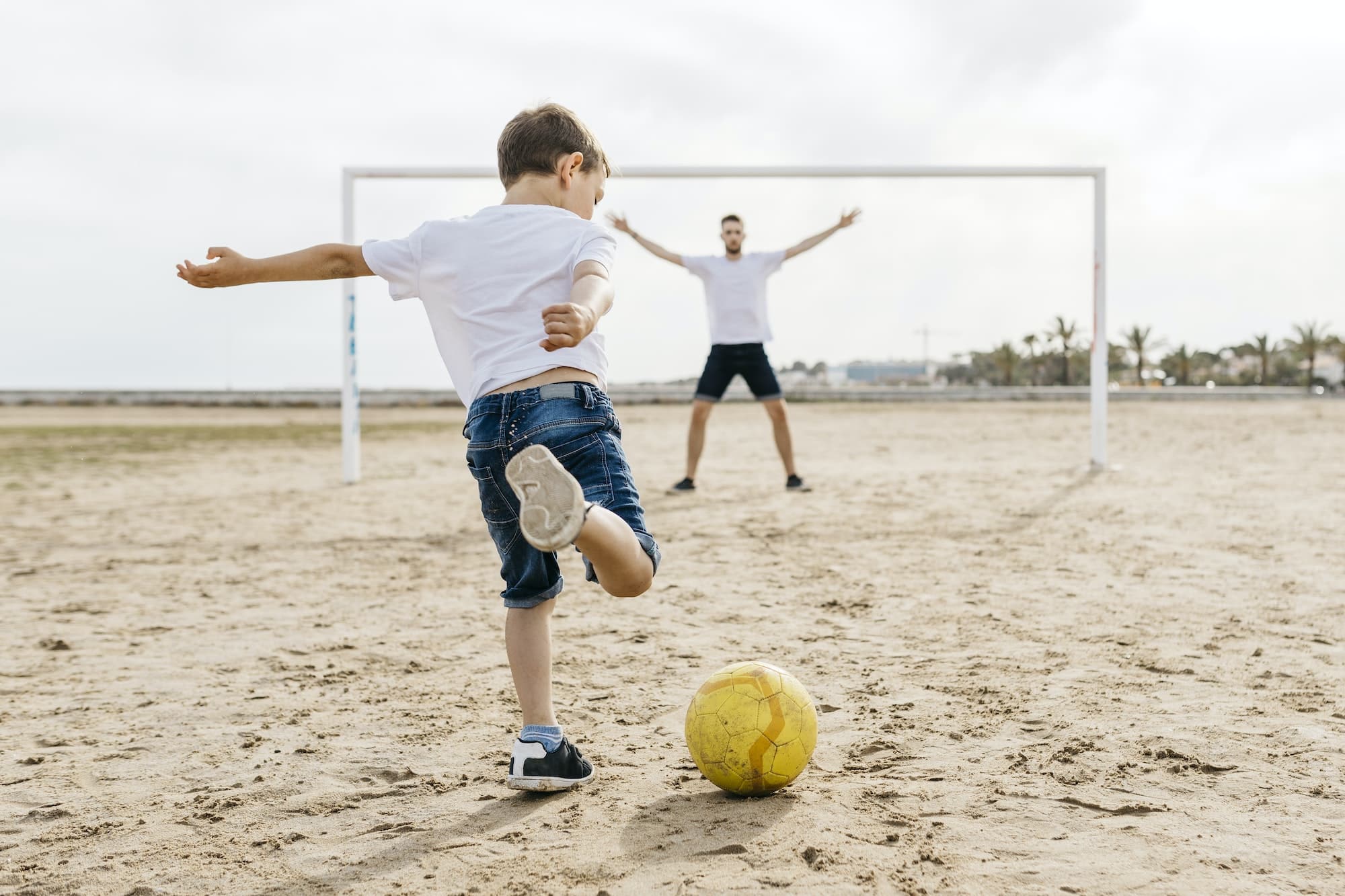 Man and boy playing soccer on the beach