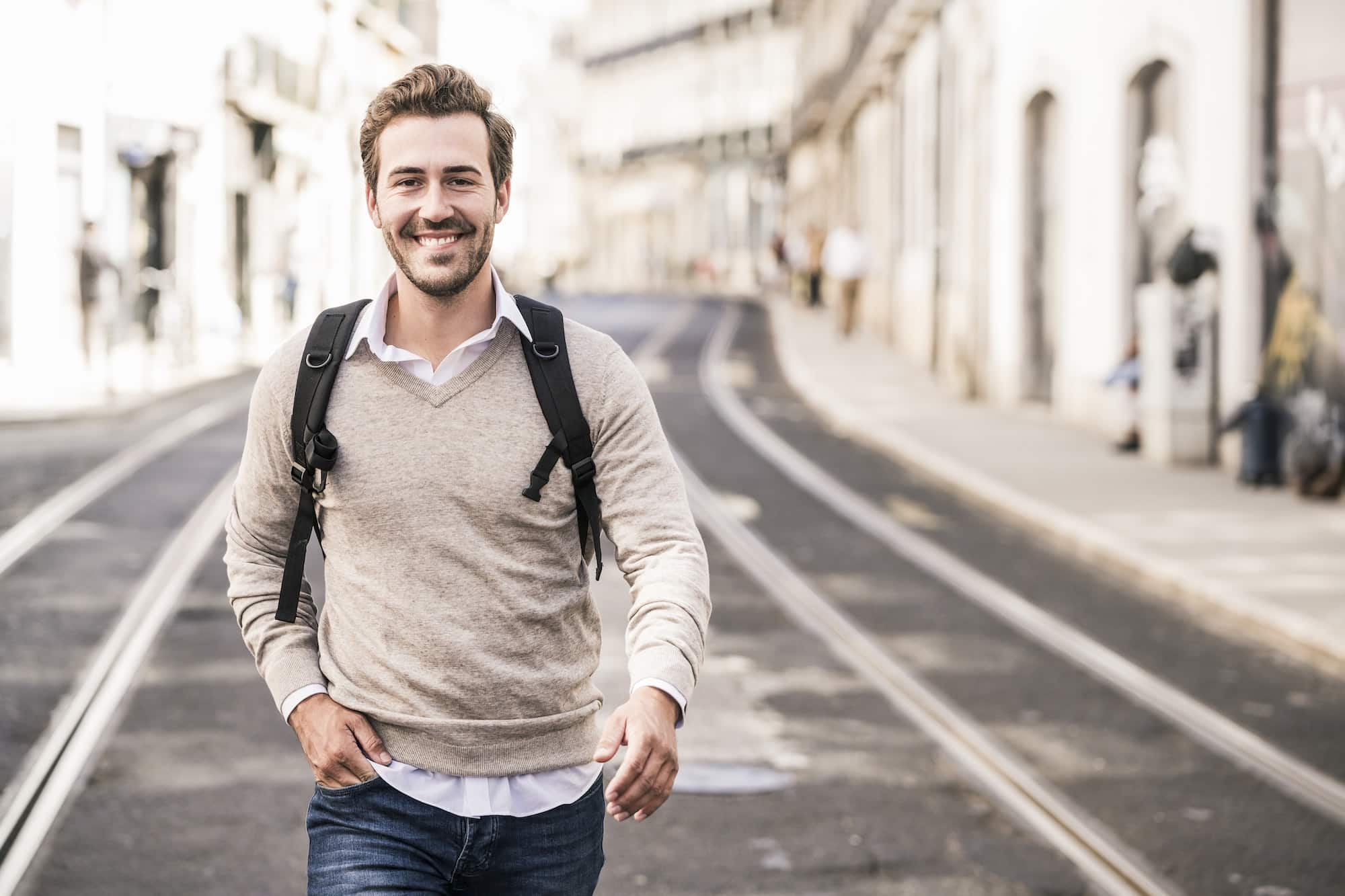 Portrait of smiling young man with backpack in the city on the go, Lisbon, Portugal