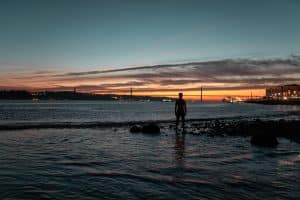 Silhouette of a young man watching the 25th of April Bridge sunset in Lisbon, Portugal