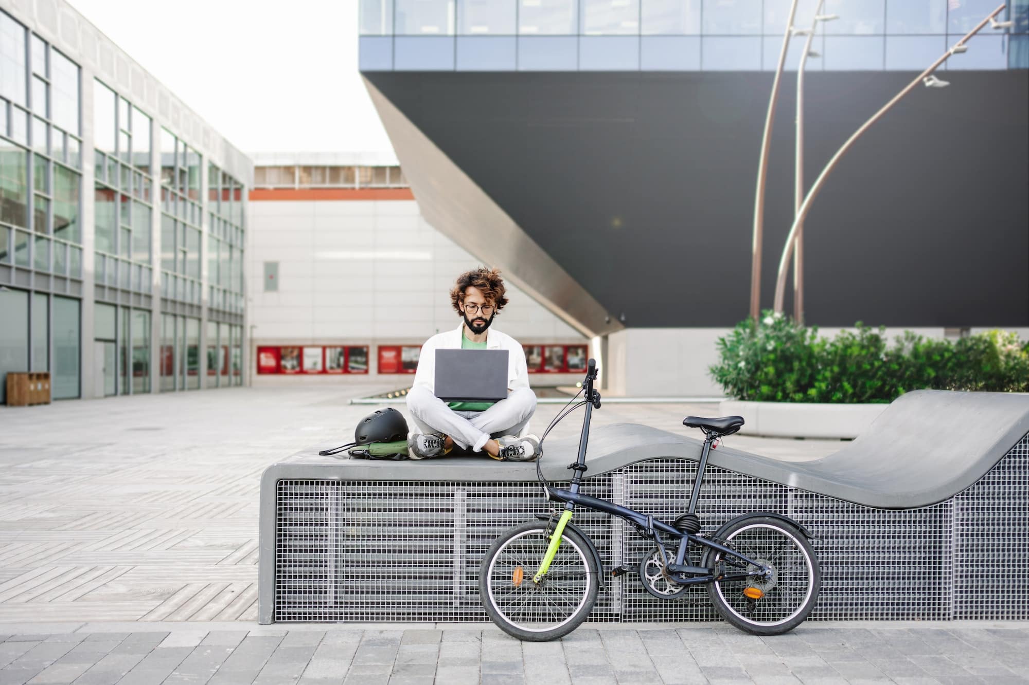 Young man working on laptop outdoors, next to bicycle - Tech Freelancer in the city