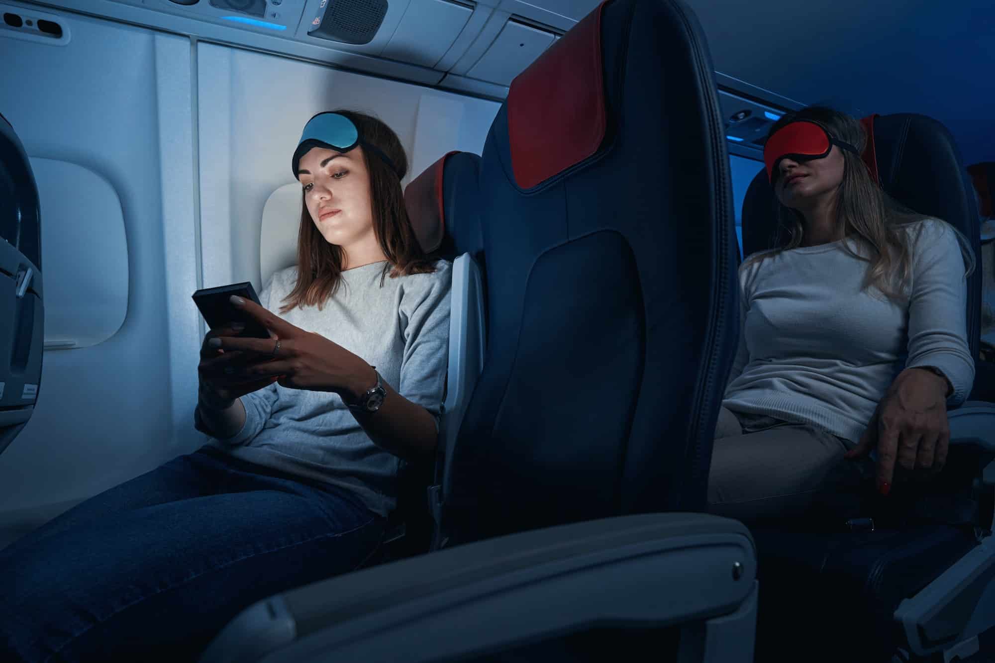 Female passenger typing on smartphone during night flight