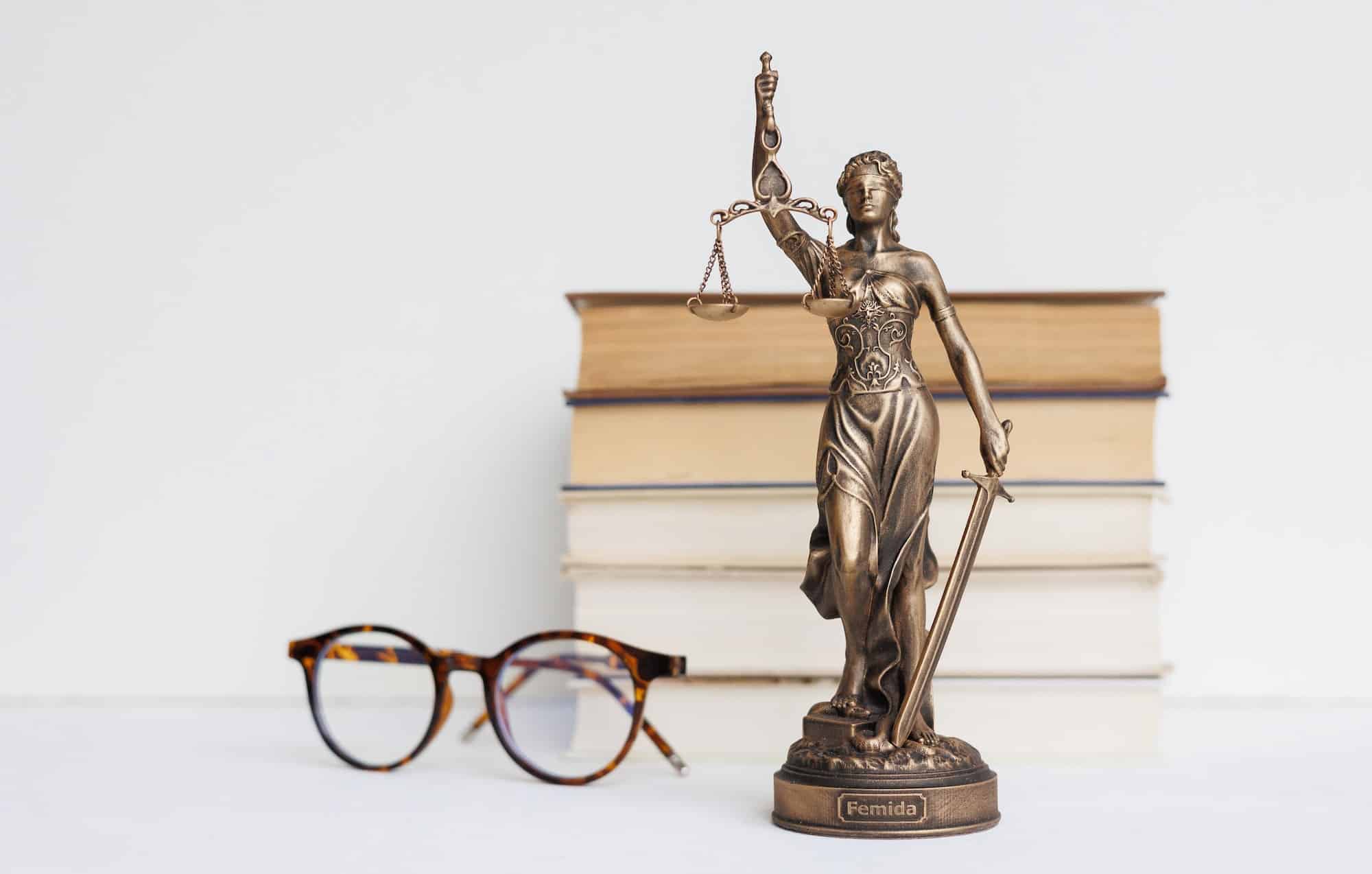 Themis goddess of justice statuette on light background on table with books and glasses.