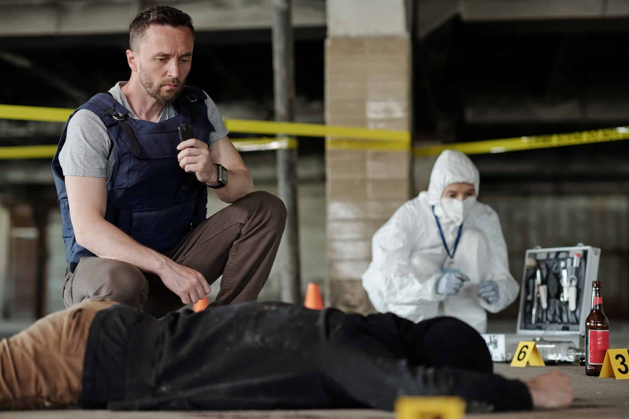 Young serious detective inspector or policeman squatting by dead body