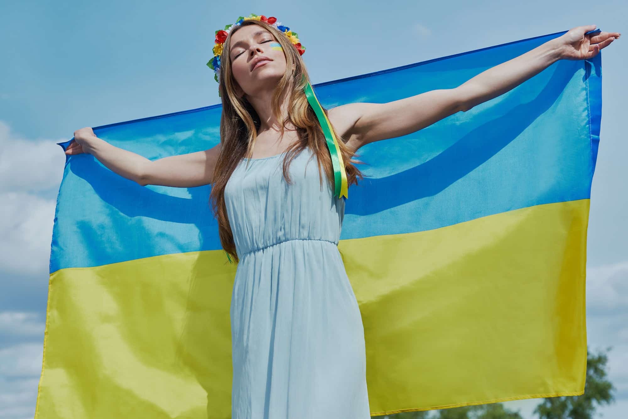 Attractive young Ukrainian woman holding national flag with sky in the background