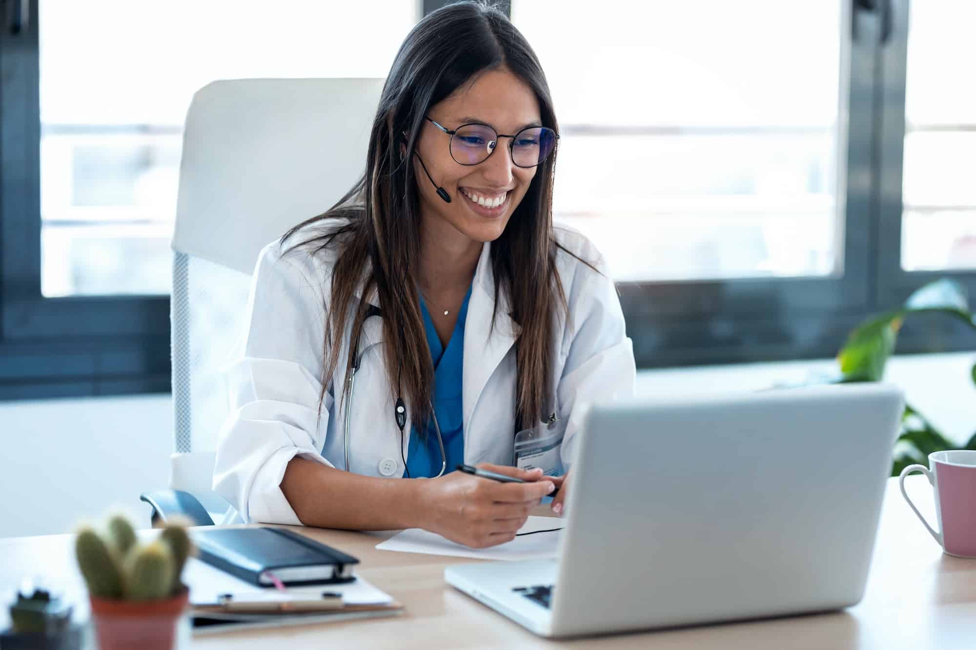 Female doctor talking with colleagues through a video call with a laptop in the consultation.