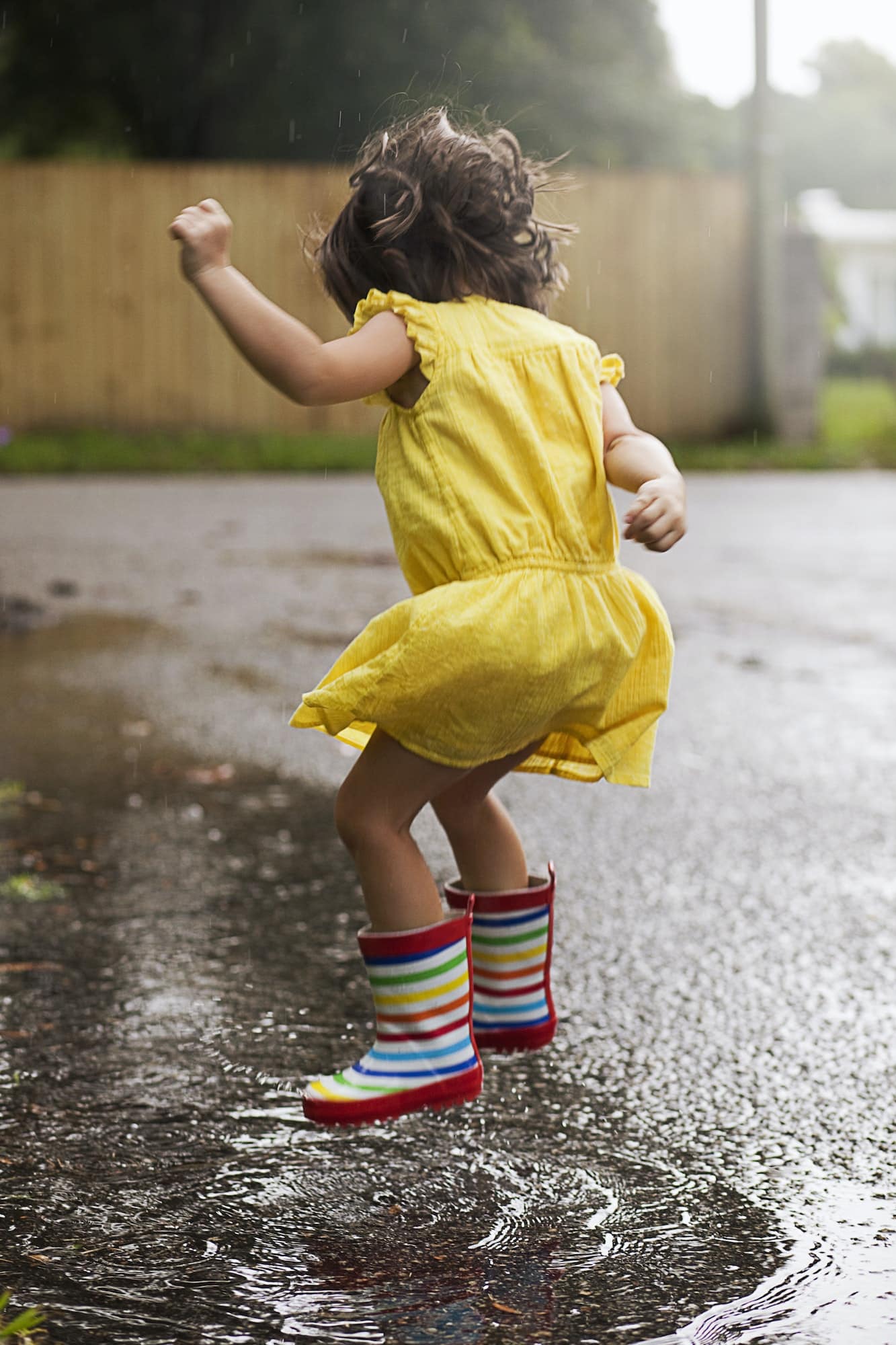 Girl wearing rubber boots jumping in rain puddle