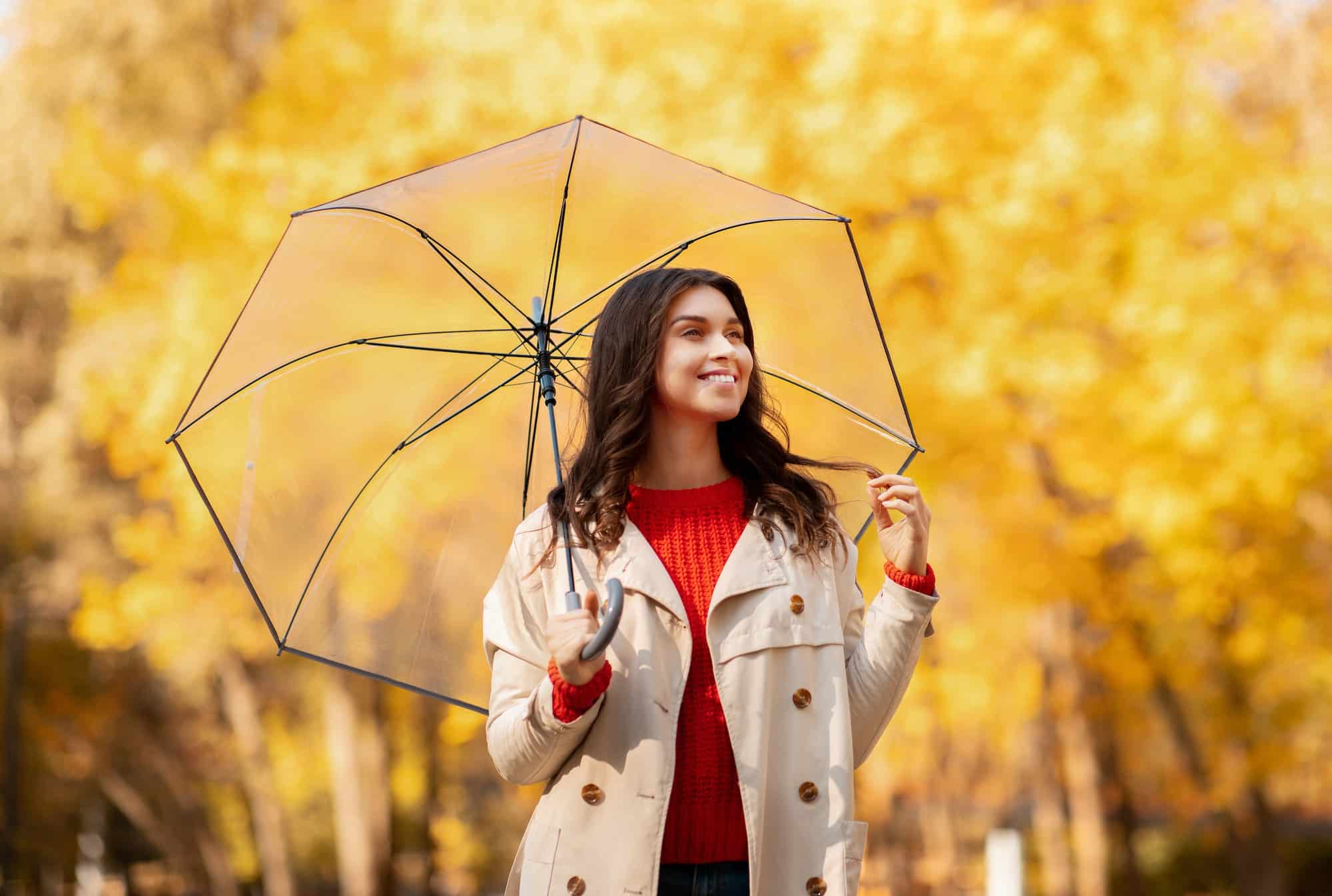 Portrait of smiling young lady in coat holding umbrella at autumn park, expecting rainfall