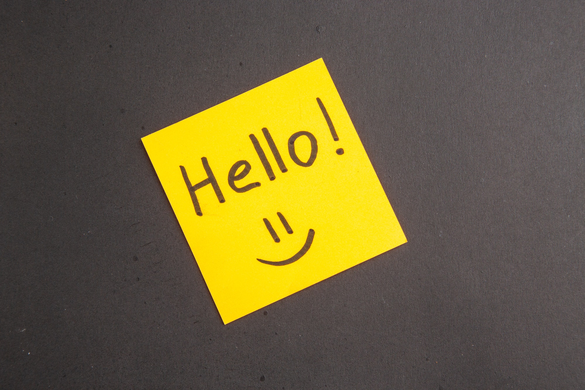 top view hello written on yellow sticky note on dark background