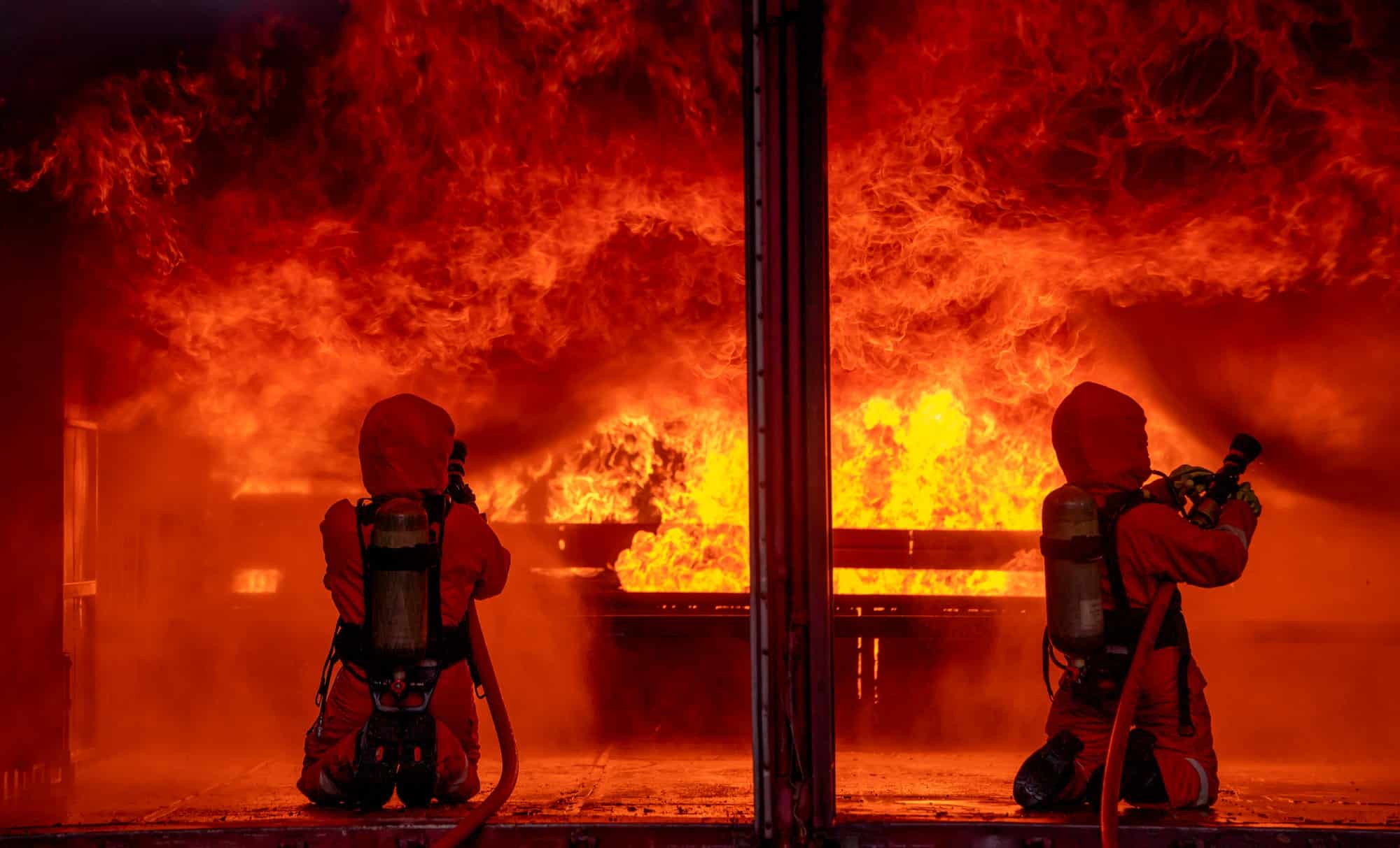 Two firefighters spray water by sprinkler to extinguish or get rid huge fire in room