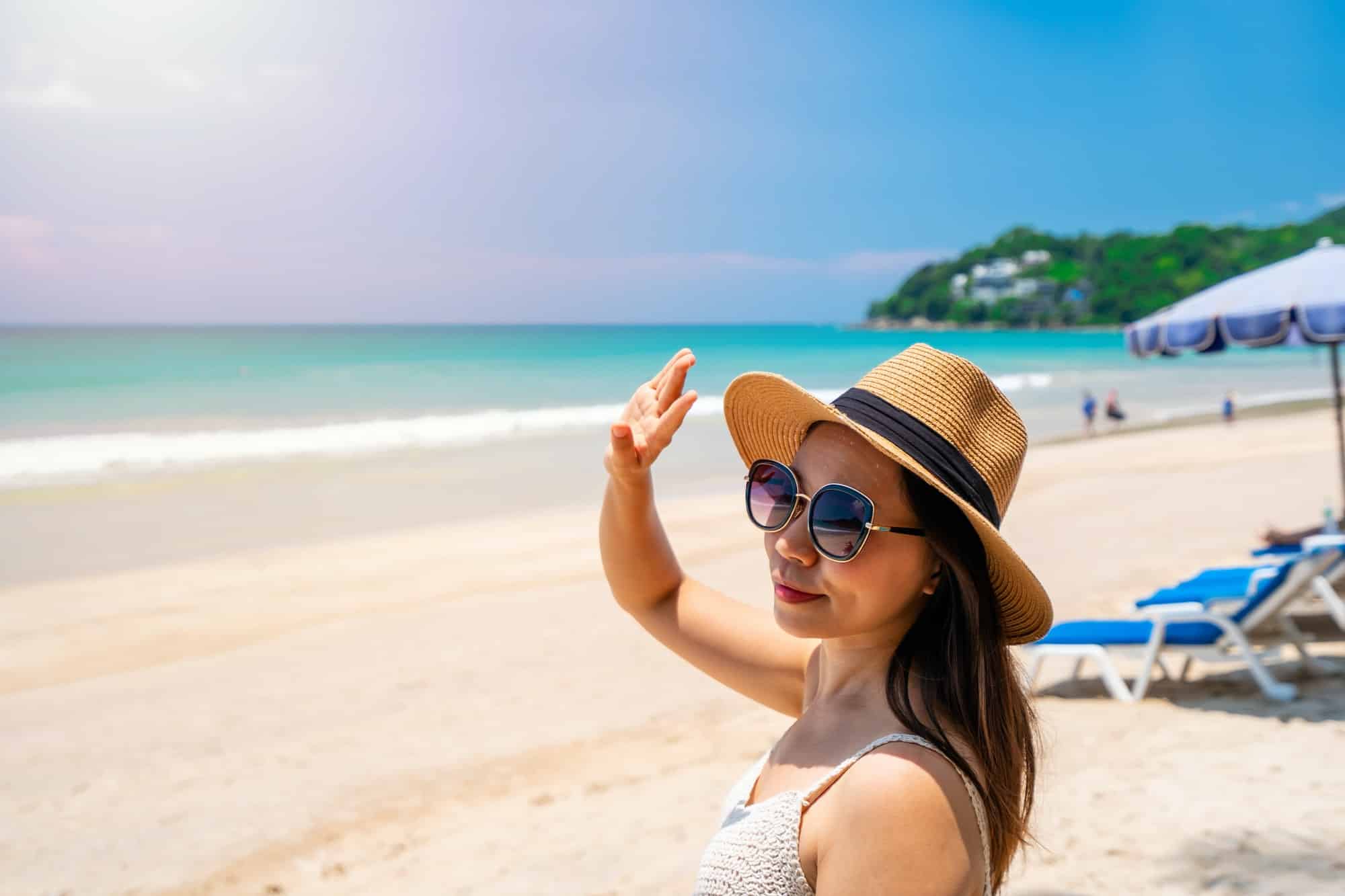 Young woman traveler wearing sunglasses covering face by hand to protect UV rays from the sun