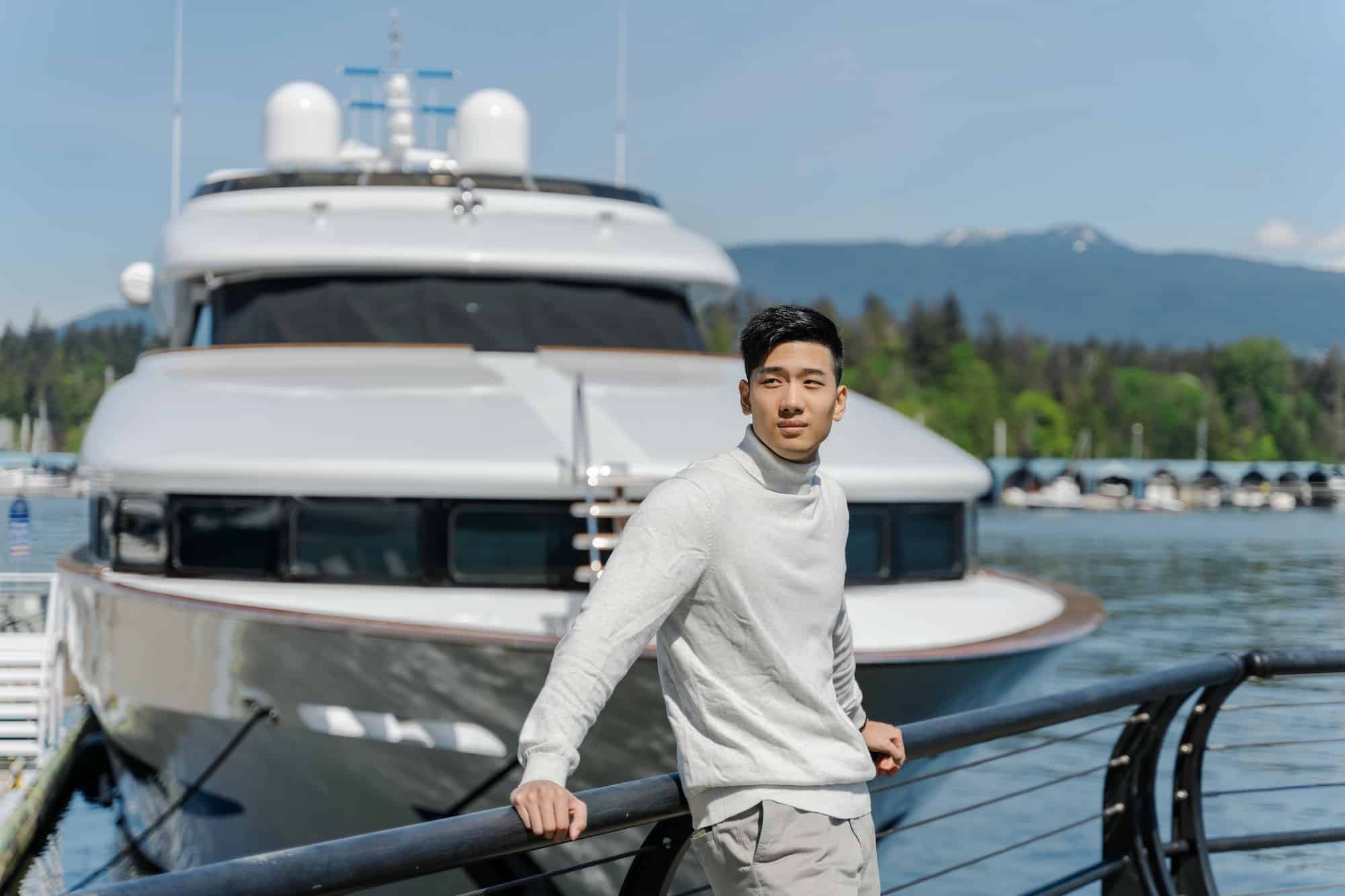 Handsome asian businessman standing near yacht, looking away. Attractive chinese businessman