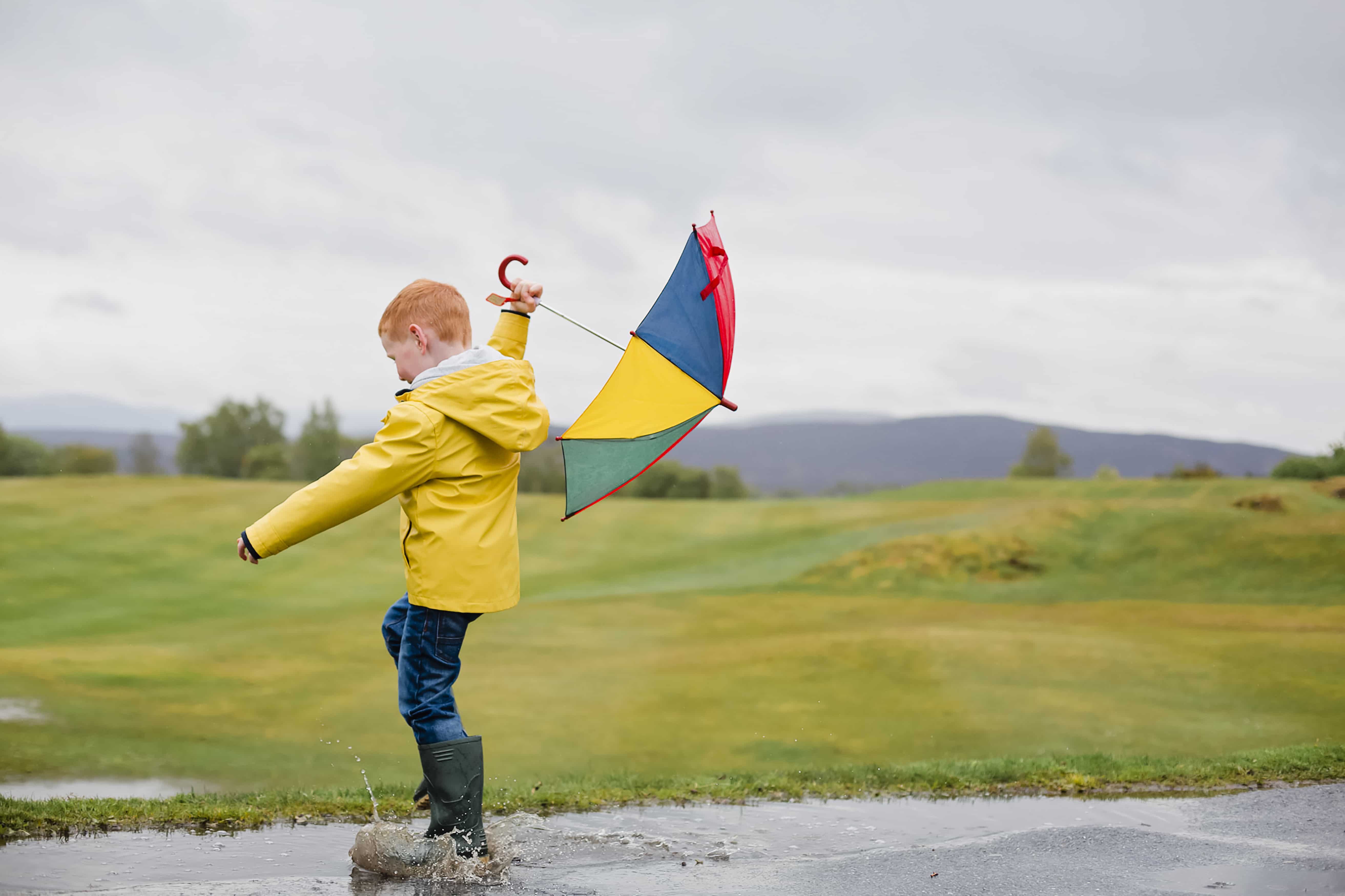 Redheaded little boy with umbrella playing in the rain