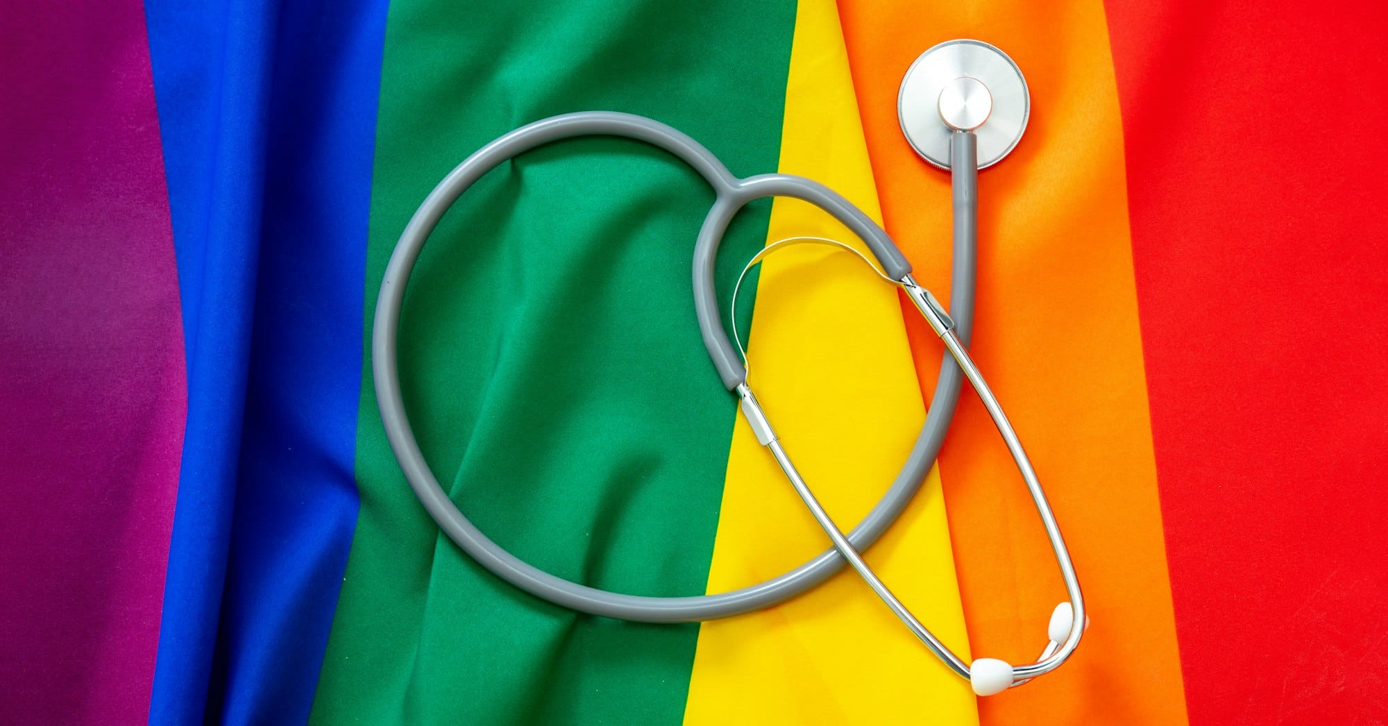 LGBT Health care. Medical Stethoscope on rainbow pride flag background, overhead view