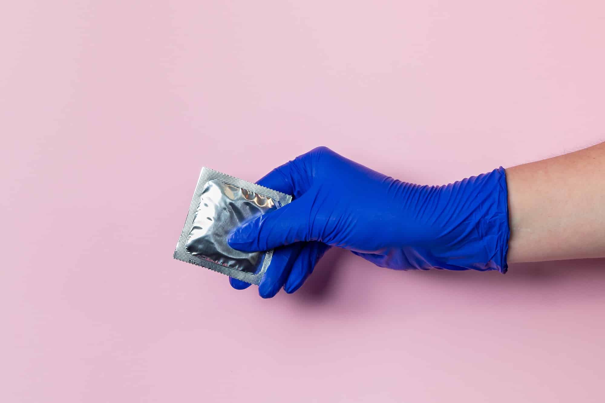 A hand in a blue latex glove holds a condom.