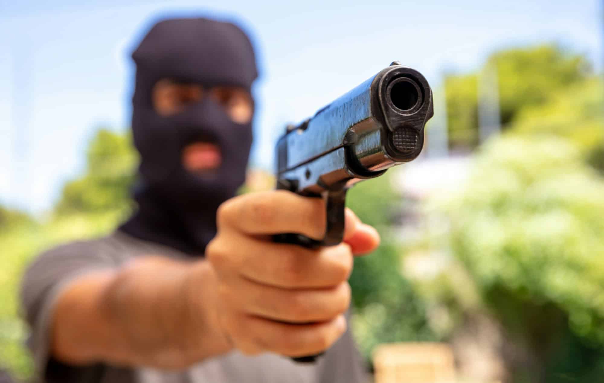 Hooded robber hand holding a pistol, blur background,