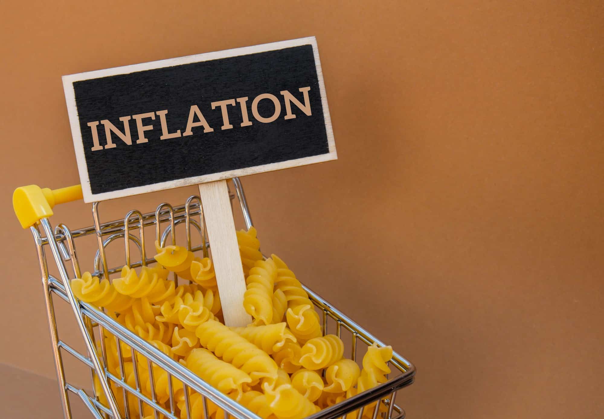 INFLATION text on Blackboard label against Shopping trolley cart Filled With Pasta on Beige