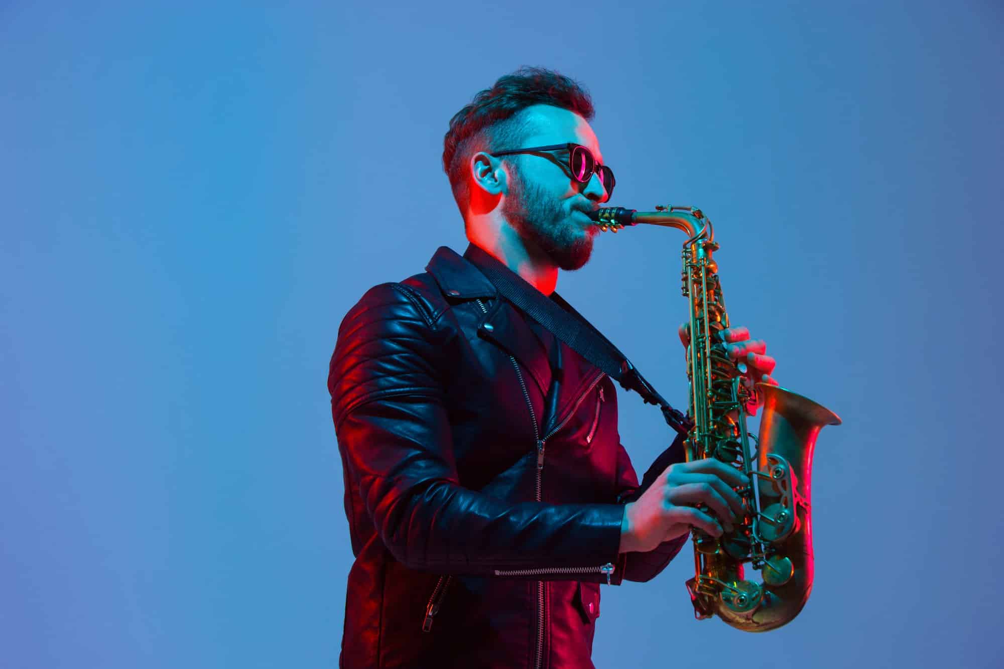 Young caucasian jazz musician playing the saxophone in neon light