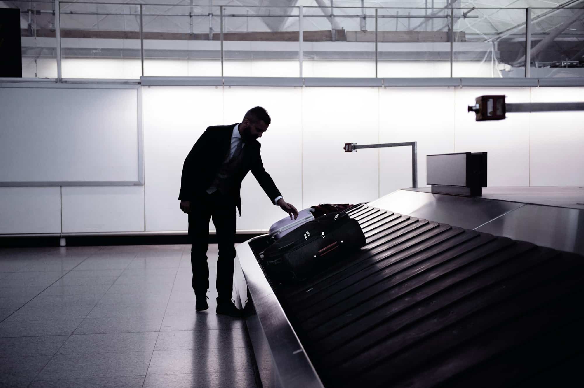 Businessman picking up suitcase on luggage conveyor belt, airpor