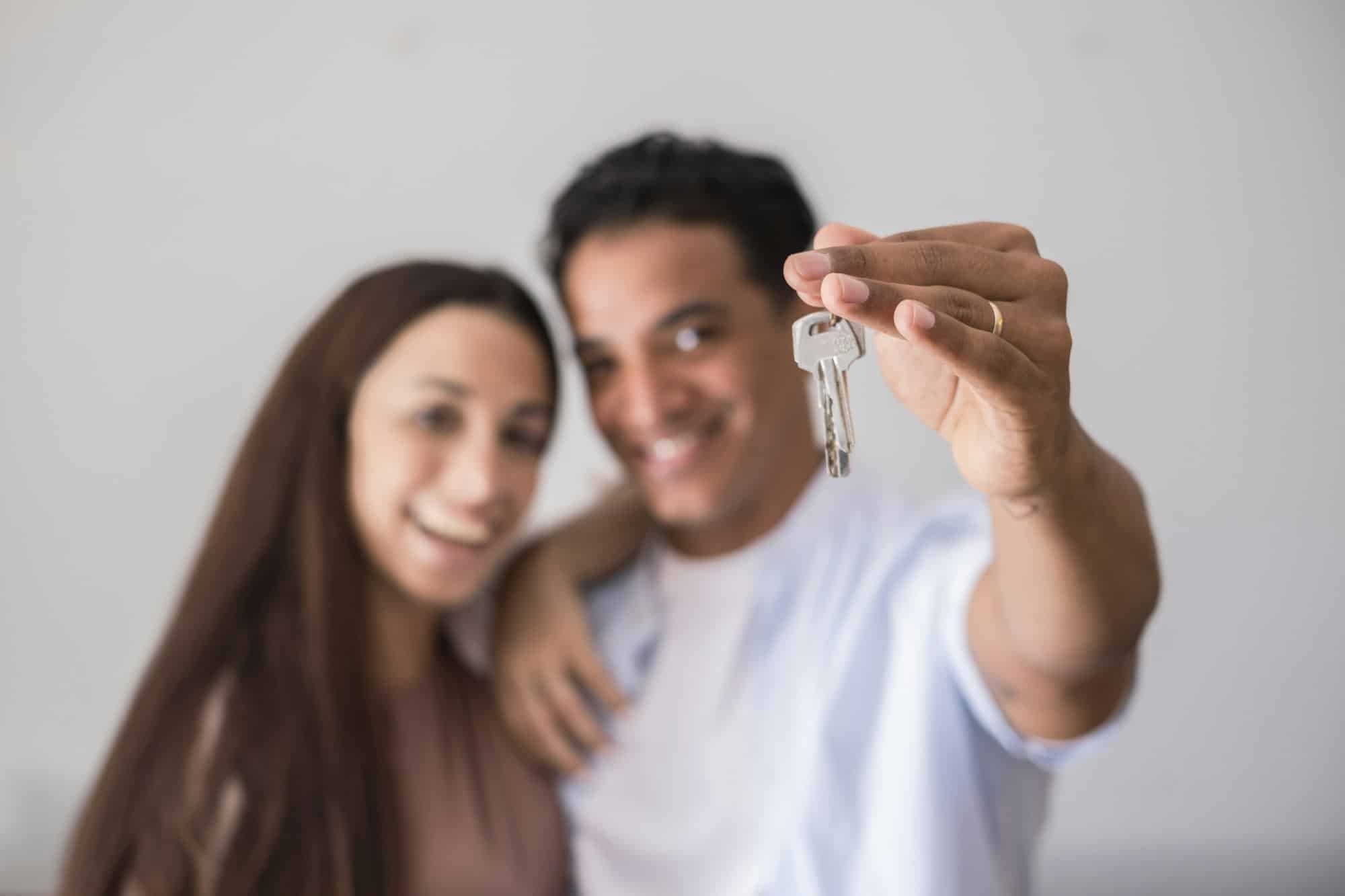 Close up of new home keys and young interracial couple smile and show the property - new life