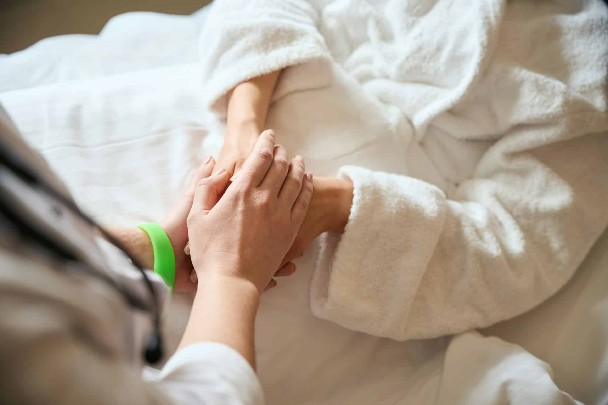 Woman with green bracelet consoles female patient in hospital room